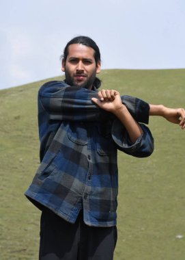 Front view of a young guy doing Cross Body Shoulder Stretch exercise in outdoor. A Indian guy warm up with Shoulder cross arm stretch pose.