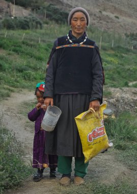 Padum, Zanskar, Kargil - Bölge, Ladakh, Hindistan - 07 19 2022: Orta yaşlı bir Ladakhi (Zanskar) kadını kızıyla birlikte geleneksel kıyafetlerini giymiş, dışarıda dururken kameraya bakıyor
