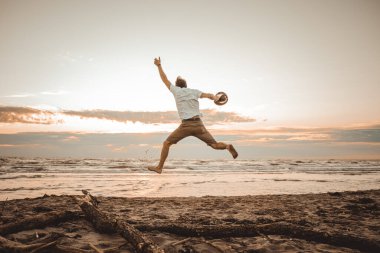 Mutlu çocuk yaz tatillerini gün batımında sahilde geçiriyor genç adam güneşin doğuşunda plajda zıplıyor.