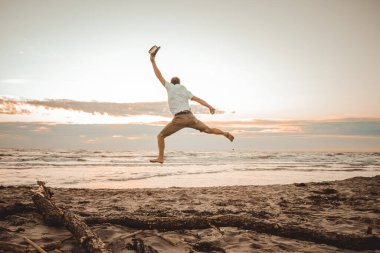 Mutlu çocuk yaz tatillerini gün batımında sahilde geçiriyor genç adam güneşin doğuşunda plajda zıplıyor.