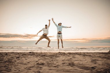 Mutlu arkadaşlar yaz tatillerini gün batımında kumsalda geçiriyorlar - iki çocuk güneşin doğuşunda plajda zıplıyor - tatil kavramı