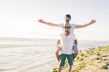 İki erkek arkadaş gülüyor, gülüyor ve sahilde eğleniyorlar. 