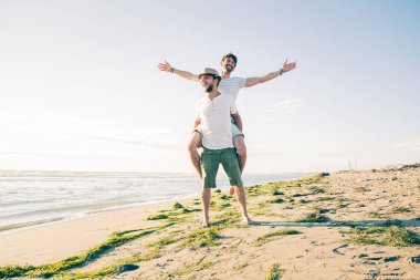 İki erkek arkadaş gülüyor, gülüyor ve sahilde eğleniyorlar. 