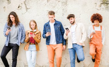 Dışarıda cep telefonu kullanan çok kültürlü bir arkadaş grubu internete girip duvarın yanında duran akıllı telefonları tutan öğrenciler.