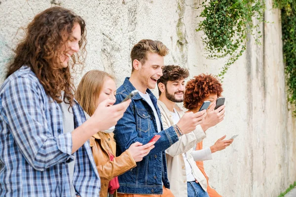 携帯電話を屋外で使用している友人の多文化グループ 壁の横に立って携帯電話のスマートフォンを保持インターネットを閲覧学生 — ストック写真