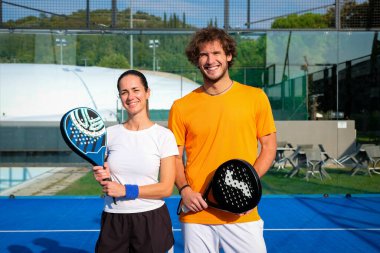 Padel sahasında raketlerle poz veren iki gülümseyen sporcunun portresi - Padel oyuncuları maçı kazandıktan sonra kameraya bakıyorlar