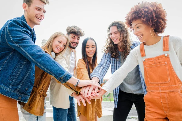 Portrait of happy university friends stacking hands together, showing unity and togetherness - Diverse Culture Students Celebrating Together - Friendship concept