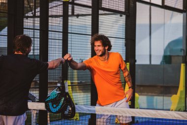 İki padel oyuncusu birbirini selamlıyor yumruk tokuştururken Padel 'in arkadaşları covid sırasında merhaba diyor.