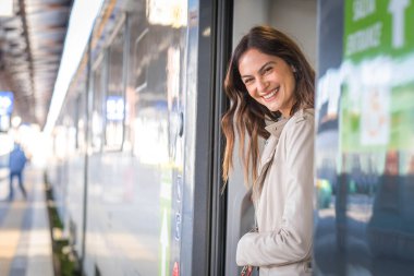 Trenden inerken gülümseyen güzel bir gezgin kadın ve tren kapısından bakan genç bir iş kadını. 