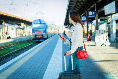 Zarif elbiseli bir kadın tren istasyonunda bekliyor. Zaman geçirmek için akıllı telefon kullanıyor. Seyahat ve iş kadını kavramı