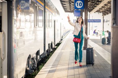 Güzel kız istasyonda koşuyor ve treni kovalıyor. El sallıyor ve trene binmek için acele ediyordu. - Bavullu genç iş kadını onsuz ayrılmadan önce trene yetişmek için koşuyordu.