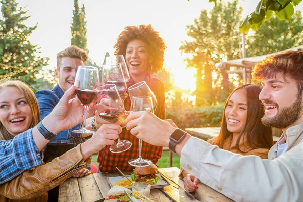 Sağlıklı yaşam tarzını sürdüren, gülümseyen ve şakalaşan bir grup arkadaş açık bar restoranında kırmızı şarap içerken, gençler bardaki indirimli içki saatlerinde şarap kadehlerini kaldırıyorlar.