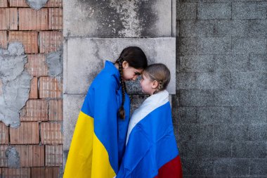 Ukrayna ve Rus bayraklı küçük kızlar bombalarla yıkılmış bir duvarın önünde. Ukrayna Rusya çatışması 2022 'de kızışıyor. Ukrayna ve Rus halkı arasında barış kavramı