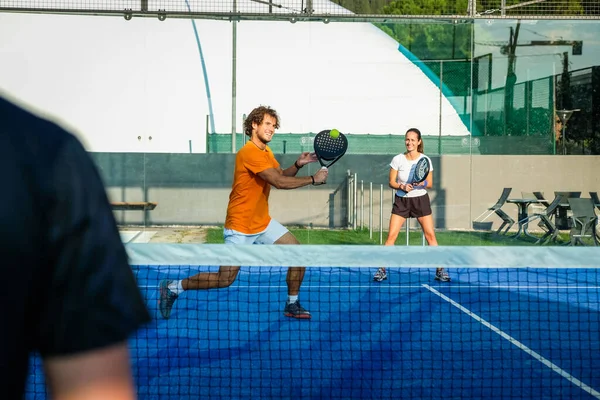 Trainer teaches young people how to play padel on outdoor tennis court - Mixed padel match outdoorin a blue grass padel court - Sport and friends concept