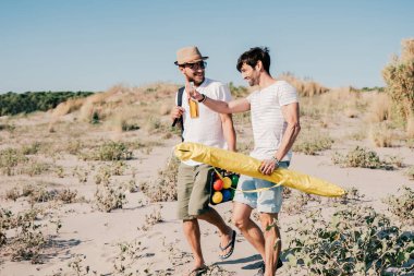 Yaz kıyafetleri içinde bir grup gülen genç arkadaş kumsalda pikniğe gidiyorlar.