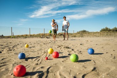 Turistler aktif bir oyun oynuyor, Petanque deniz kenarındaki kumlu bir sahilde - plaj tatillerinde bulvarda oynayan bir grup genç - toplar yerde