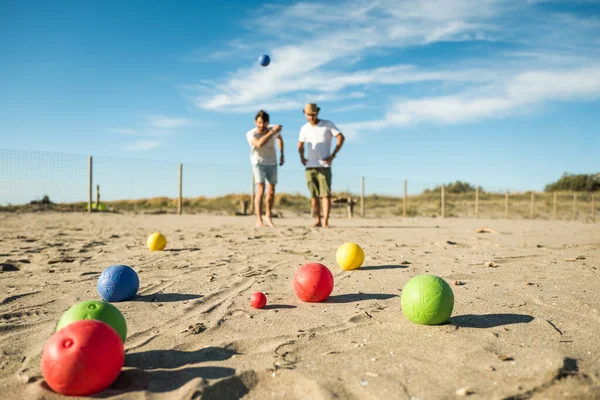 Tourists play an active game, petanque on a sandy beach by the sea - Group of young people playing boule outdoors in beach holidays - Balls on the ground
