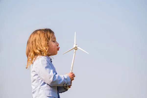 Closeup of little boy blowing a wind turbine toy and studying how green energy works from a young age - Concept of future generation and enewable Energy