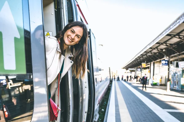 站在火车站门口偷窥某人的年轻女商人 乘坐火车的漂亮女旅行者的画像 旅行的概念 免版税图库照片