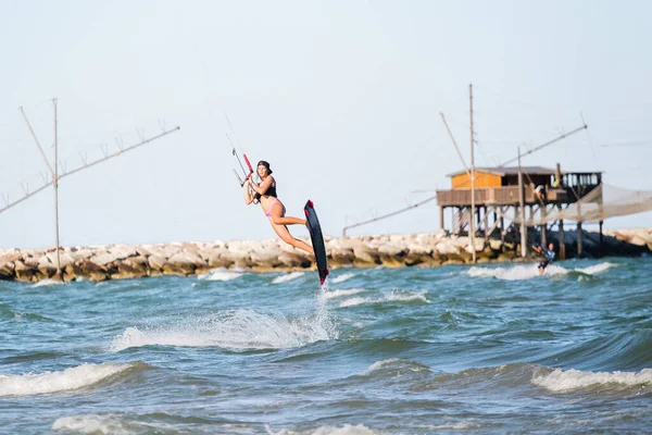 Kite surfing girl in swimsuit with kite in the sky rides the waves with splashing water. Water sports, sporty woman, action concept and hard sport