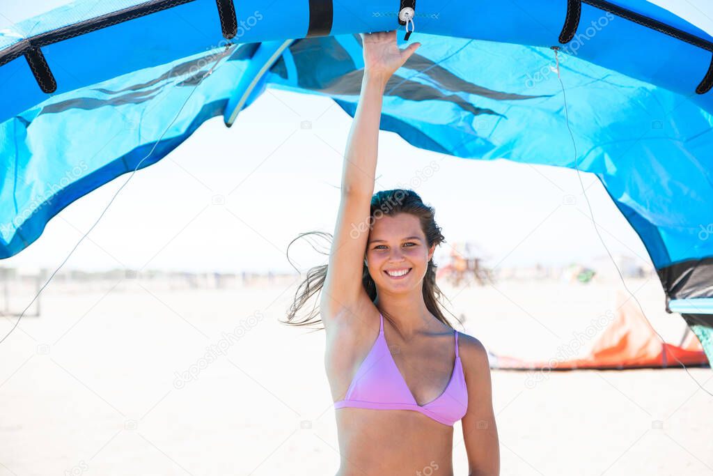 Beautiful kite surfing girl in pink bikini swimsuit, holding a kite in his hand standing on the beach for a good kiteboarding session