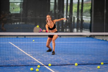 Kapalı alanda padel oynayan bir kadın genç sporcu kadın raketle topa vuruyor.