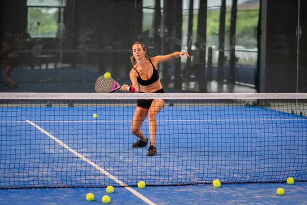 Kapalı alanda padel oynayan bir kadın genç sporcu kadın raketle topa vuruyor.