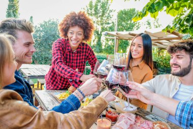 Group of multiracial friends taking selfies and celebrating with wine glasses at dinner time in terrace - Young people eating and drinking red wine at the outdoor rooftop bar  and taking selfie using mobile smartphone