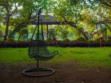 Rattan hasır koza bahçe salıncak sandalyesi bir bahçede asılmış.