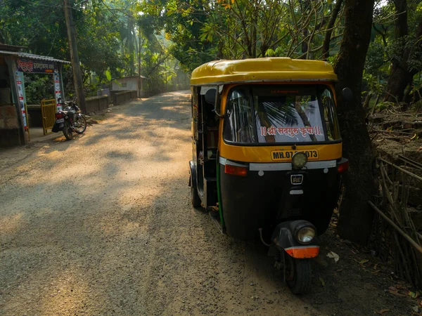 Malvan, INDIA - 19 Aralık 2021: Konkan 'da Hindistan cevizi ağaçlarıyla çevrili küçük bir Hint köyünün Picturesque sokağındaki bir yolda duran otomobil rickshaw.