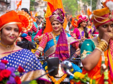 Mumbai, India - April 02, 2022: A beautiful indian female dressed in traditional attire driving a bike during a procession celebrating Gudhi Padva or Hindu new year in Mumbai