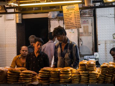 Mumbai, India - May 1, 2022 : Muslim male vendor baking and selling fresh breads from roadside stall at night market in holy month of Ramadan or Ramazan at Bhendi Bazar.