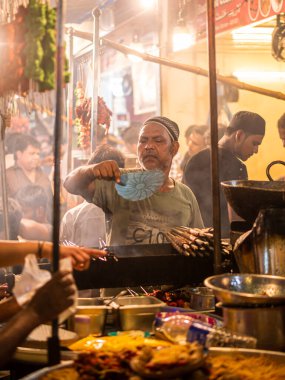 Mumbai, India - May 1, 2022 : Muslim male vendor cooking selling halal foods and Kababs from roadside stall at night market in holy month of Ramadan . Vertical or portrait orientation