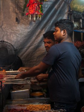Mumbai, India - May 1, 2022 : Muslim male vendor cooking selling halal foods and Kababs from roadside stall at night market in holy month of Ramadan . Vertical or portrait orientation