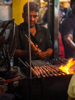 Mumbai, India - May 1, 2022 : Muslim male vendor cooking selling halal foods and Kababs from roadside stall at night market in holy month of Ramadan . Vertical or portrait orientation