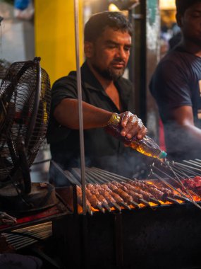 Mumbai, India - May 1, 2022 : Muslim male vendor cooking selling halal foods and Kababs from roadside stall at night market in holy month of Ramadan . Vertical or portrait orientation