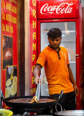 Mumbai, India - May 1, 2022 : Muslim male vendor cooking selling halal foods and Sweets like Jalebi from roadside stall at night market in holy month of Ramadan . Vertical or portrait orientation