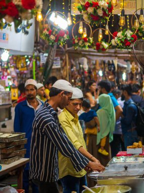 Mumbai, India - May 1, 2022 : Muslim male vendor cooking selling halal foods and varous sweets from roadside stall at night market in holy month of Ramadan . Vertical or portrait orientation