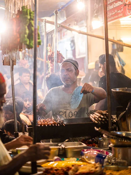 Mumbai, India - May 1, 2022 : Muslim male vendor cooking selling halal foods and Kababs from roadside stall at night market in holy month of Ramadan . Vertical or portrait orientation