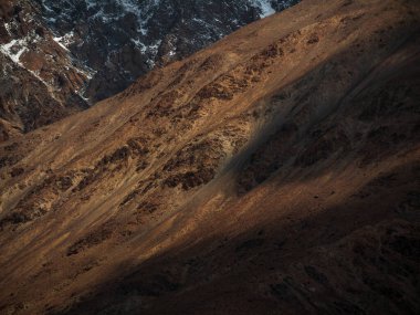 Güneş ışığıyla kaplı bir dağ yamacında taş dokusu. Gölgeler ve röfleler. Ladakh, Hindistan.