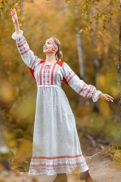 民俗伝統的なスラブの服の若い美しい笑顔の女性の肖像は秋の森の中で手で自然霊を迎え — ストック写真