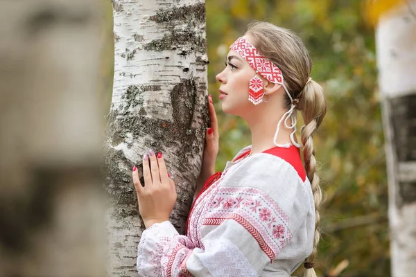 森の中で自然の中で白樺の木を抱いて民俗伝統的なスラブ服の若い美しい女性の肖像画 パガン奴隷の概念 — ストック写真