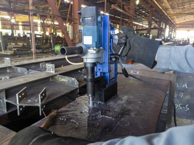 İşçiler endüstriyel fabrikada çelik kirişte delik açmak için bir Manyetik sondaj makinesi kullanıyorlar..