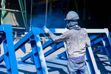 Ressam, montaj alanına gitmeden önce çelik bir yapı boyamak için sprey tabanca kullanıyor..