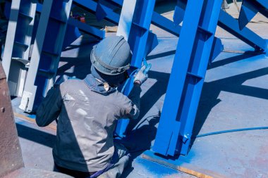 Ressam, montaj alanına gitmeden önce çelik bir yapı boyamak için sprey tabanca kullanıyor..