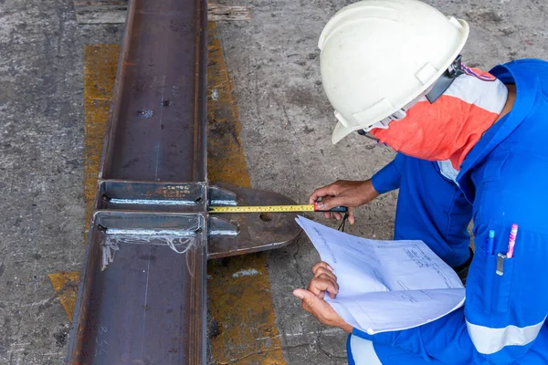 Teknisyenler, boya için teslimattan önce çelik yapının doğruluğunu kontrol etmek için bir mezura kullanıyorlar..