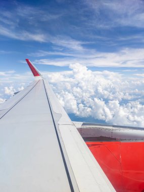 Mavi gökyüzünde uçak kanatları ve tüylü beyaz bulutlar.