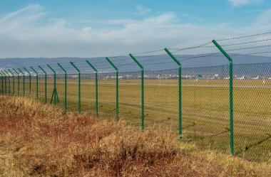 Green steel wire mesh fence around the airport area. Restricted area protection.