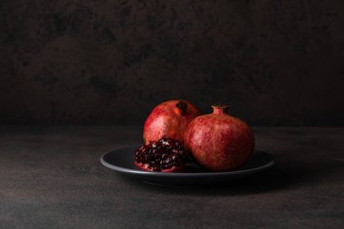 İki olgun nar ve bir tanesi gri bir tabakta koyu bir arka planda kırılmış.