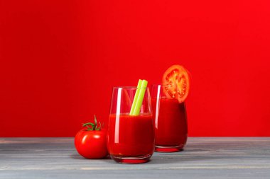 İki bardak kerevizli domates suyu ve kırmızı zemin üzerinde gri tahtalardan yapılmış bir masada duran bir domates suyu.